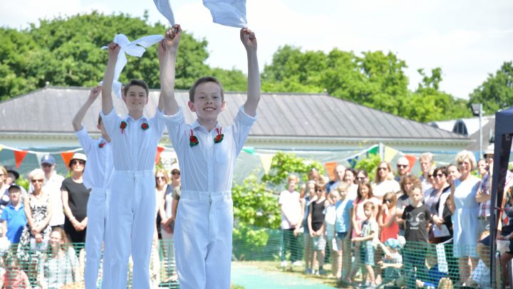 Three young boys wearing white dancing in front of a large crowd