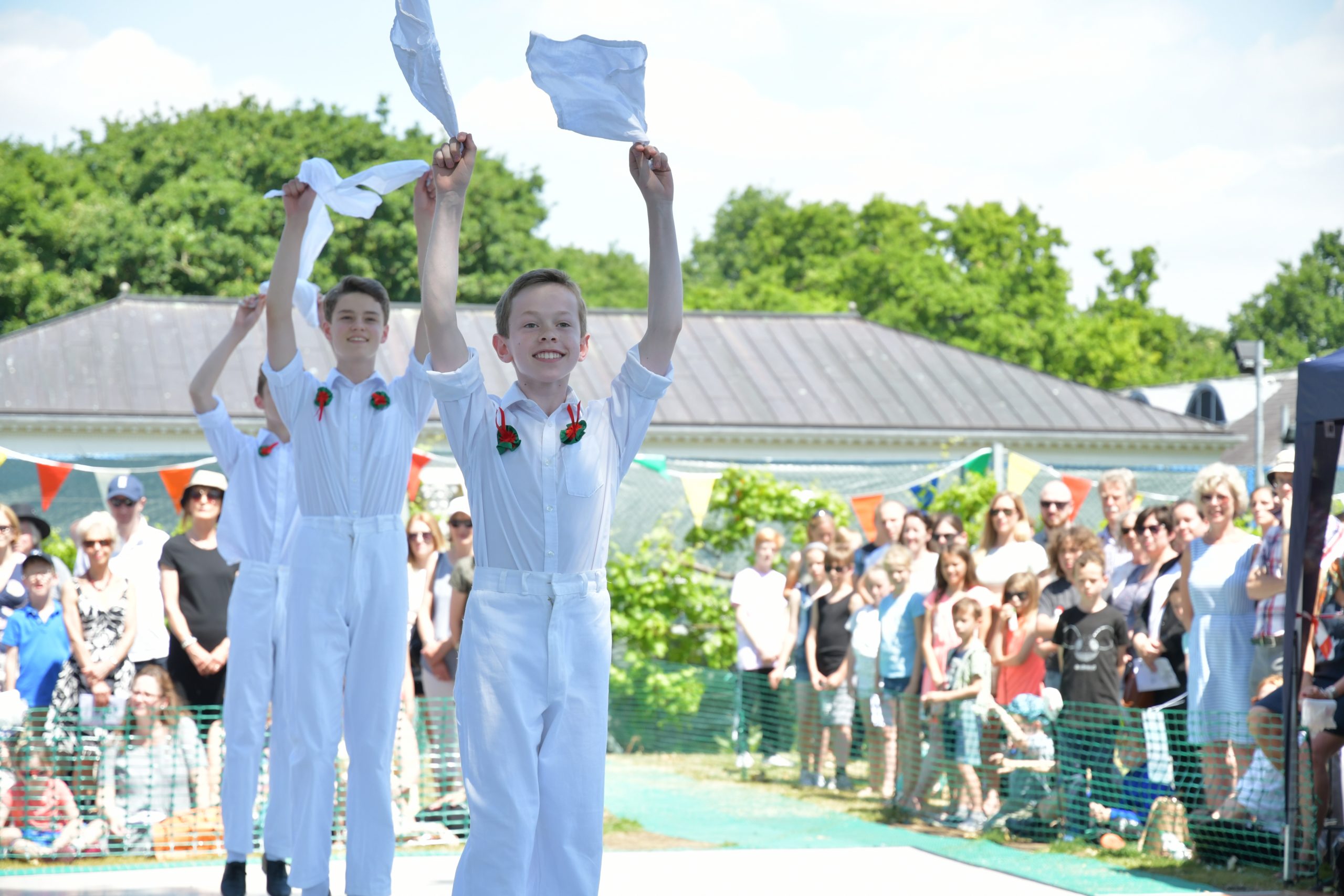 Three young boys wearing white dancing in front of a large crowd