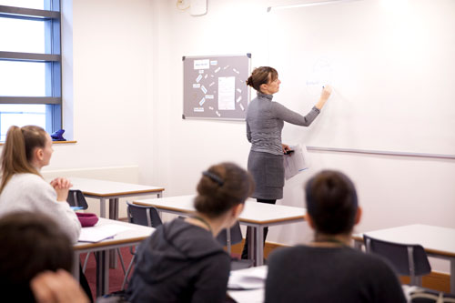 Teacher Training Manager writing on a whiteboard, teaching students in a classroom