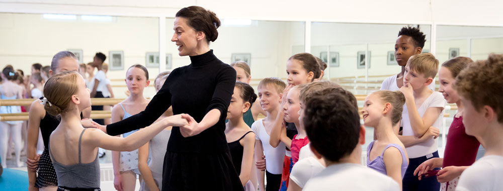 A teacher demonstrating with a student surrounded by a group of young dancers.