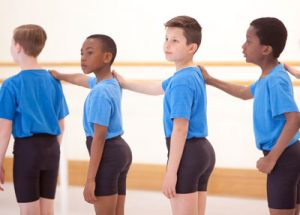 Four primary steps students stood in a line holding the shoulder of the student in front of them.