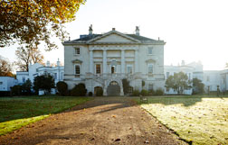 The exterior of white lodge, a grand white building, in autumn sunlight.