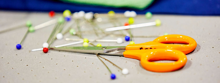 Abstract image of a pair of scissors and sewing pins on a table.