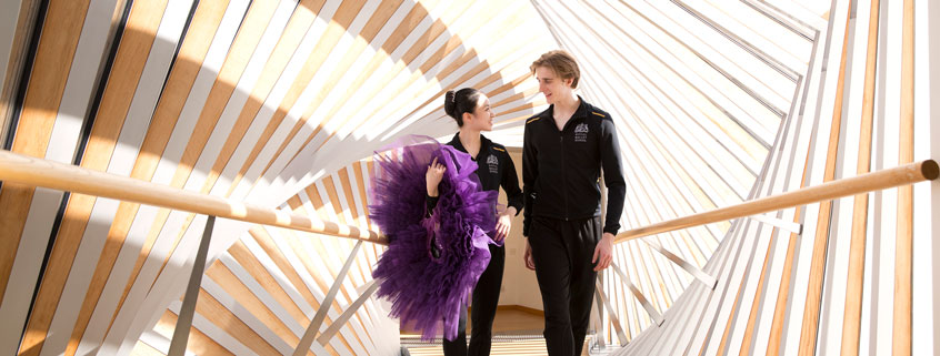 Two students walking across the bridge of aspiration, one student is holding a tutu in their hand