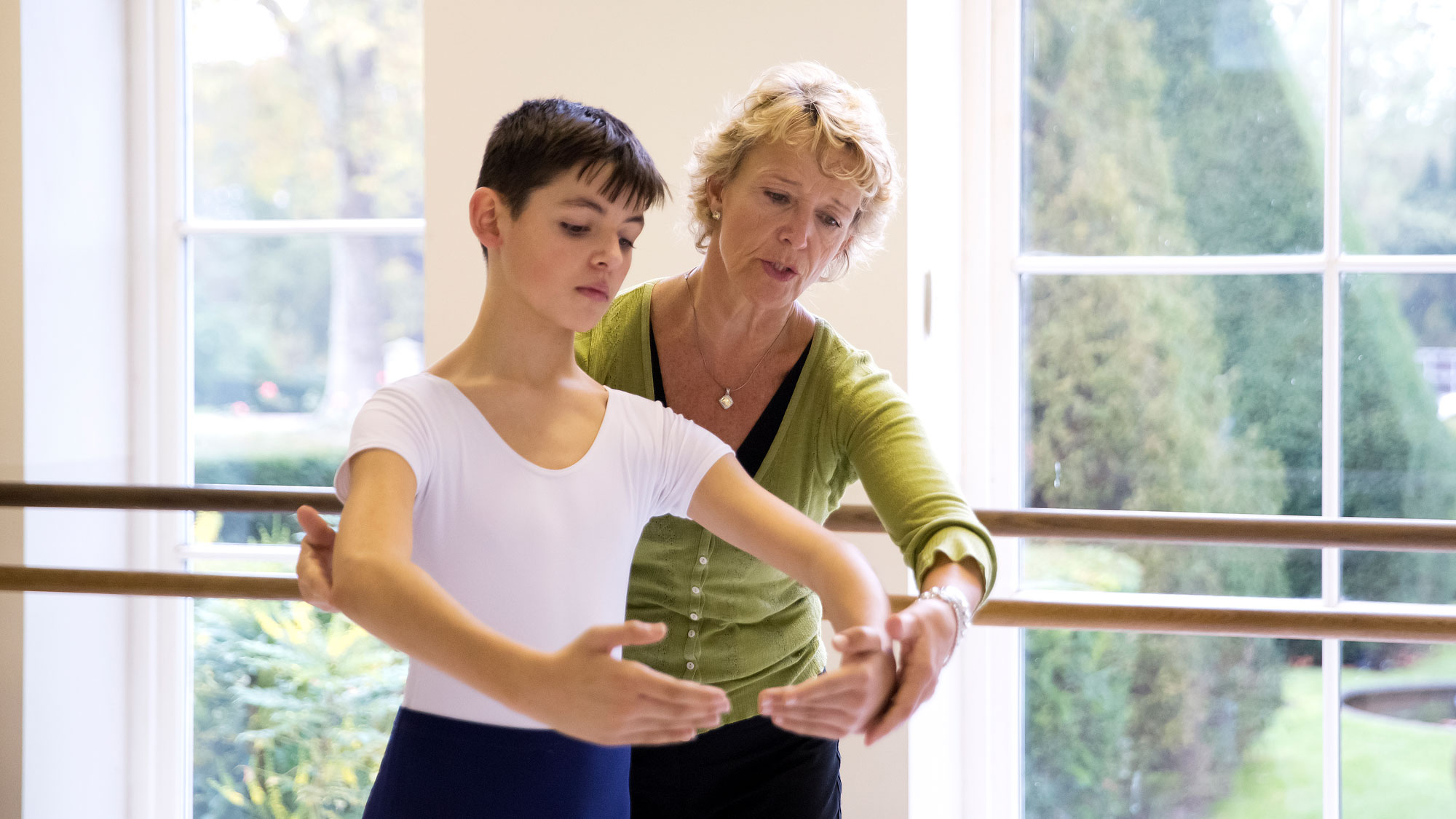 Ballet teachers behind a student doing centre work offering corrections