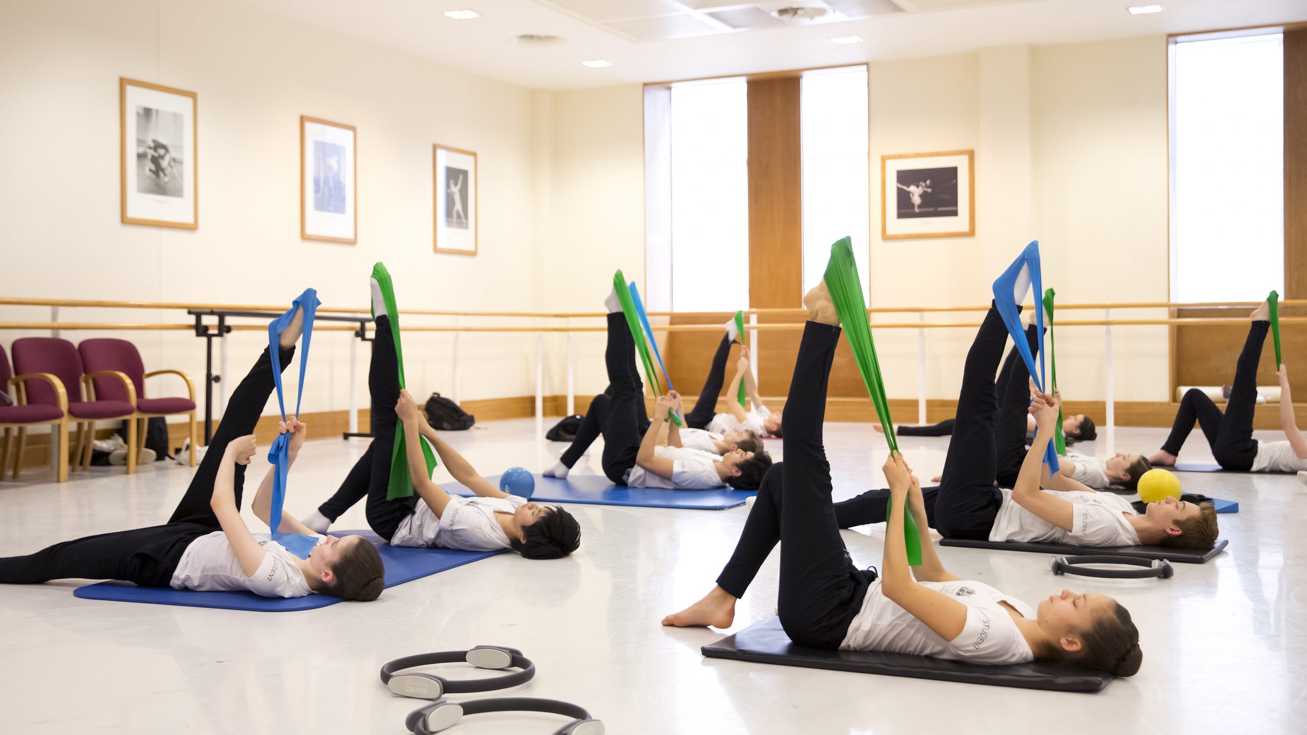 Students lying on the floor of the studio use blue and green resistance bands for training