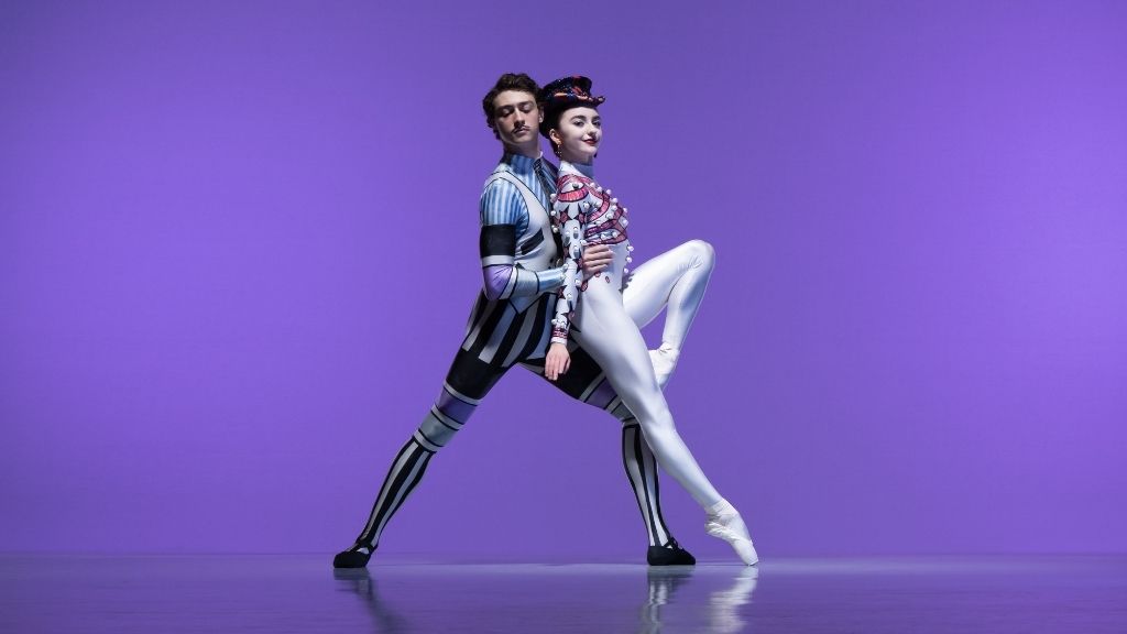 Two students in elite syncopations costumes posing in front of a purple background