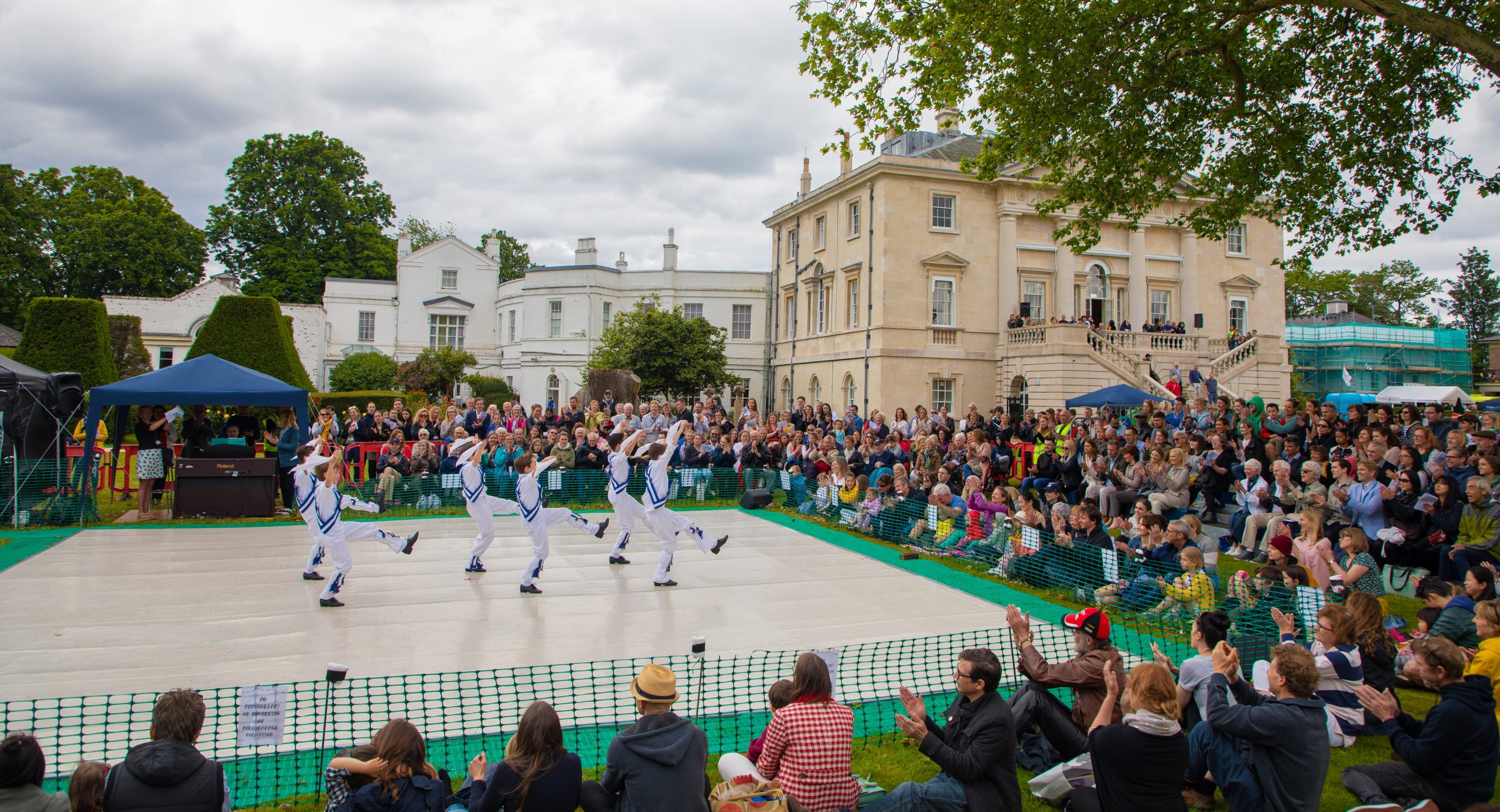 Virtual summer fair 2021 Students performing a dance on an outside stage in front of the white lodge building surrounded by a large audience