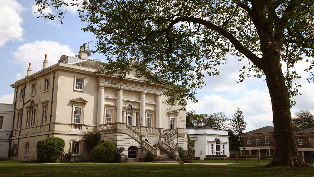 The white lodge building in the sun, surrounded by green grass and leafy trees