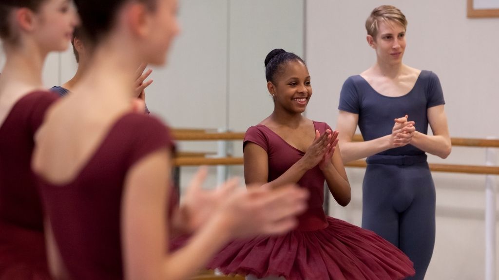 Students stand in a studio, smiling and clapping