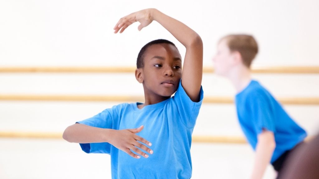 A young boy dances with one arm above his head and one in front of his torso