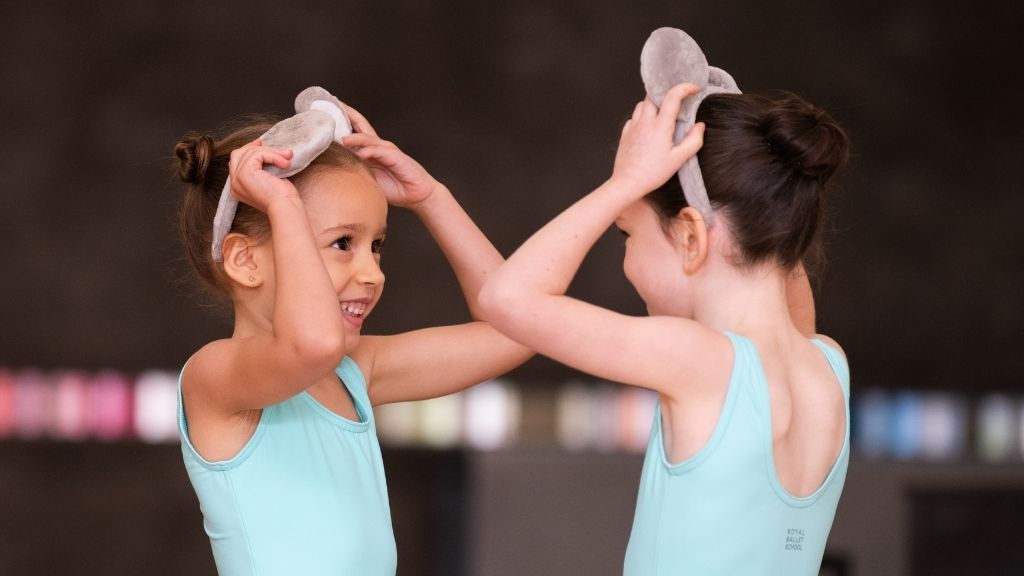 Two students wearing mouse headbands face each other smiling