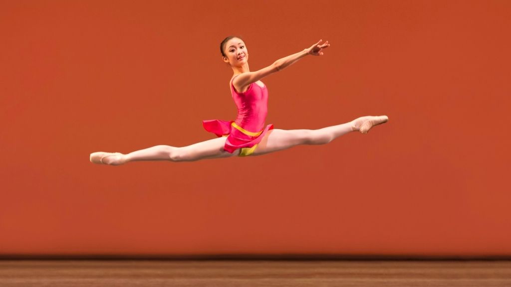 Yaoqian shang wearing a pink and yellow leotard leaps in the air