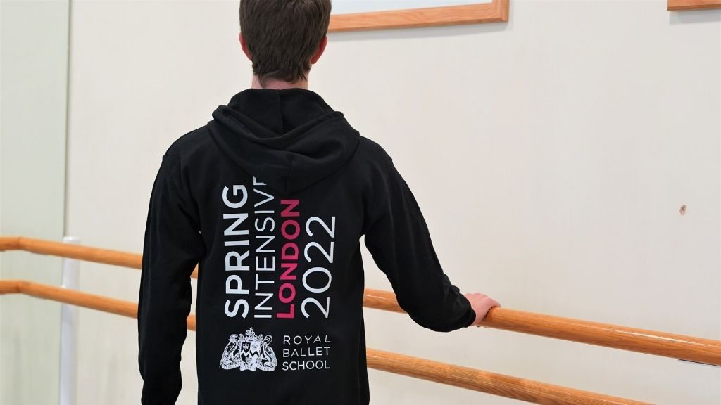 A student wearing a spring intensive 2022 hoodie in a studio holding the barre