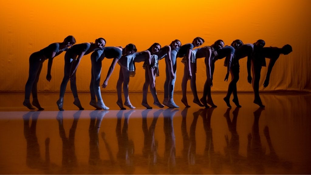 Students perform in a line, leaning forward with their heads on each others backs