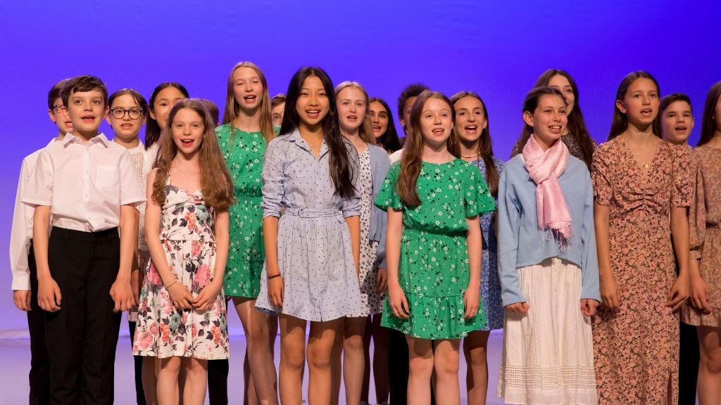 A group of young students stand in two rows, singing