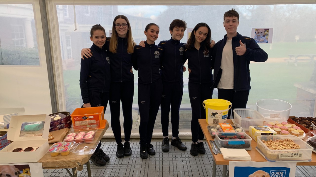 Students at a bake sale standing in front of a table of cakes