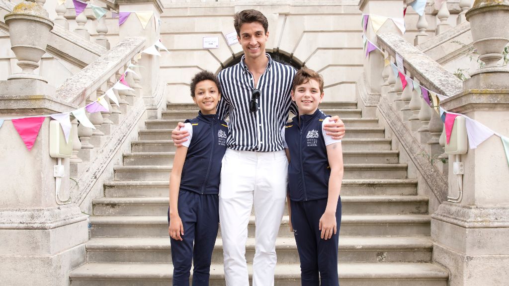 Principal of the royal ballet reece clarke stands on the white lodge steps with his arms around two white lodge students