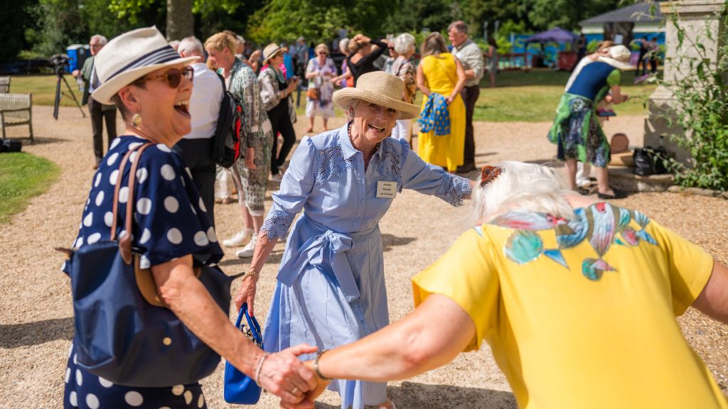 3 alumni of the royal ballet school hold hands and dance in a circle, smiling