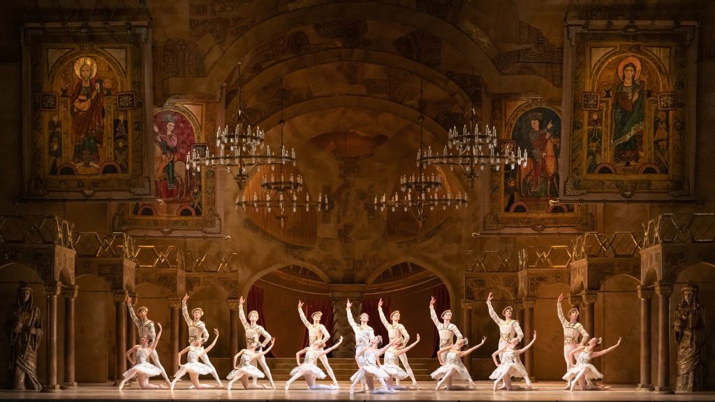 Male dancers stand in a line with female dancers kneeling in front of them on a stage