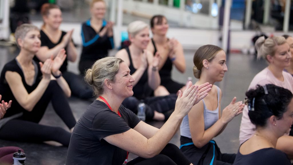 A group of trainee affiliate teachers are seated on the floor, smiling and applauding