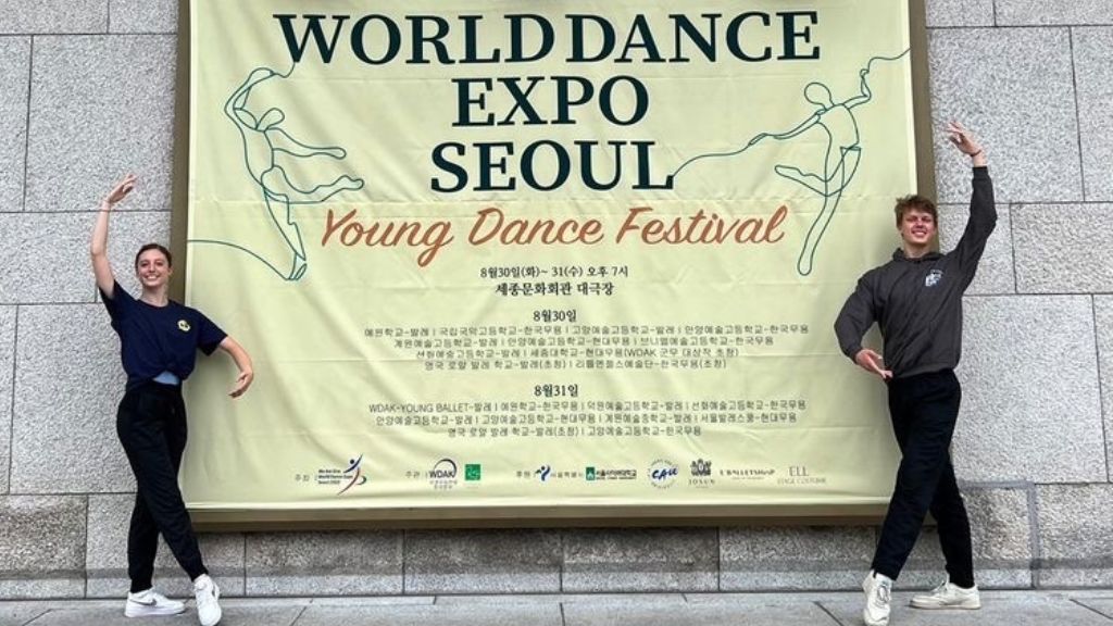 Scarlett harvey and luc foskett stand in 4th position either side of a banner advertising the young dance festival in seoul