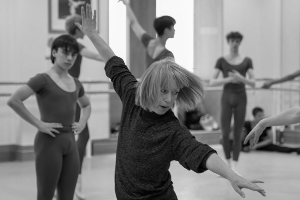 A black-and-white photograph of mikaela polley demonstrating a piece of choreography with her arms outstretched