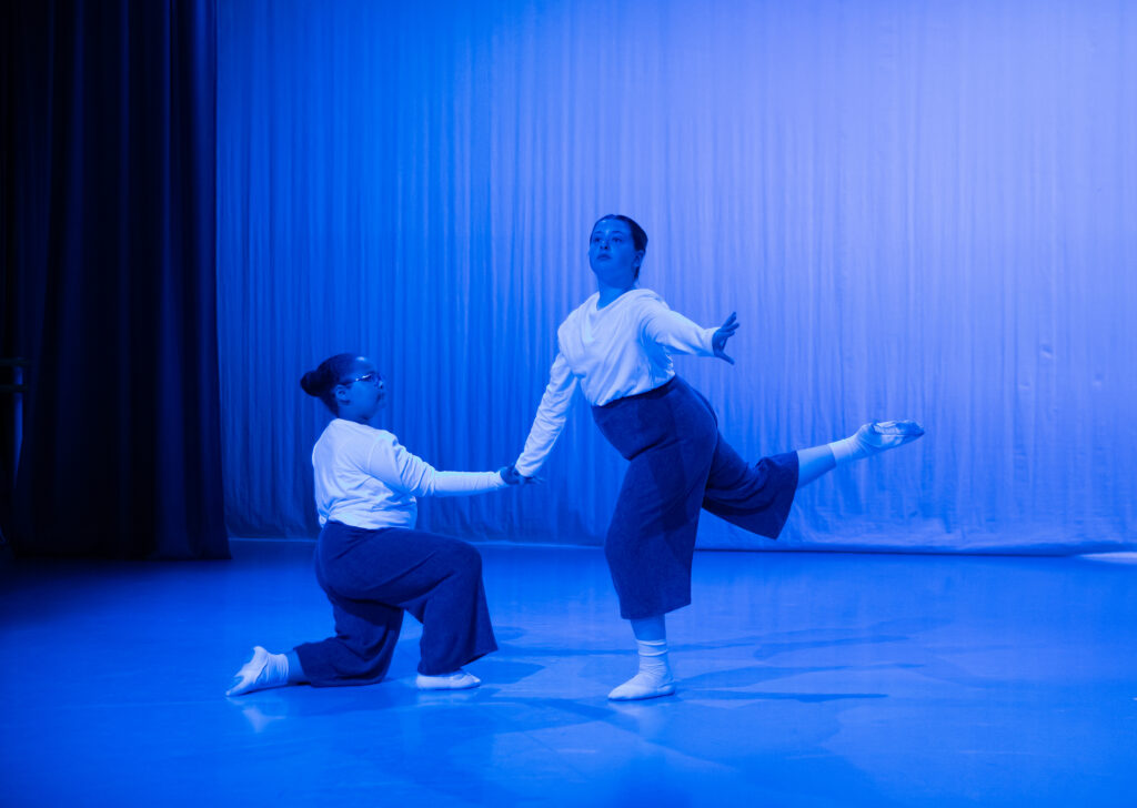 Celebrating 20 years of primary steps Two child dancers - one kneeling and the other flicking their leg up in blue lighting.