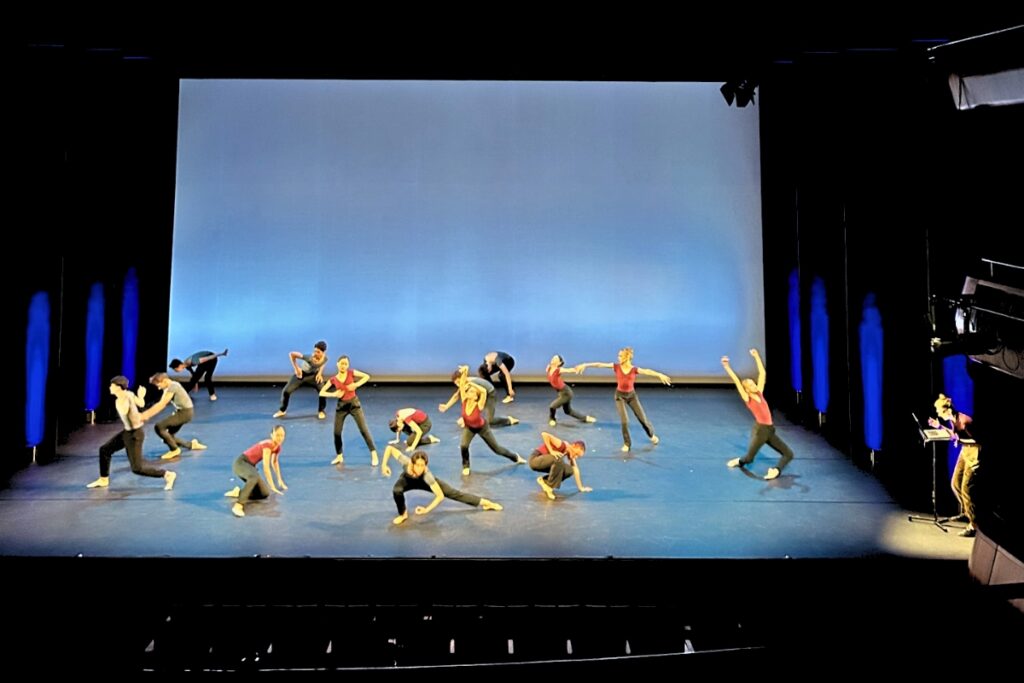 1st year students perform on stage with devon standing downstage left reading the immersive descriptive audio text