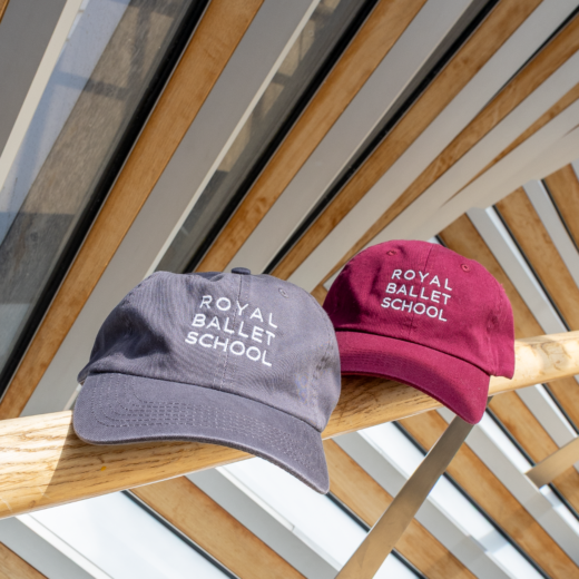 Royal Ballet School branded baseball cap in the colours burgundy and charcoal. Photographed on the Bridge of Aspiration