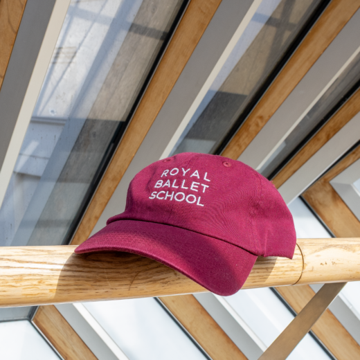 Royal Ballet School branded baseball cap in colour burgundy. Photographed on the Bridge of Aspiration
