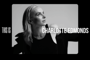 Black and white photograph of charlotte edmonds looking up, wearing a black tank top and blazer.