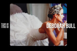 Deborah bull in a swan lake tutu and headpiece leaning on a counter and applying lipstick