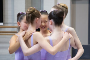 Year 7 girls in light purple leotards hug in a circle and smile