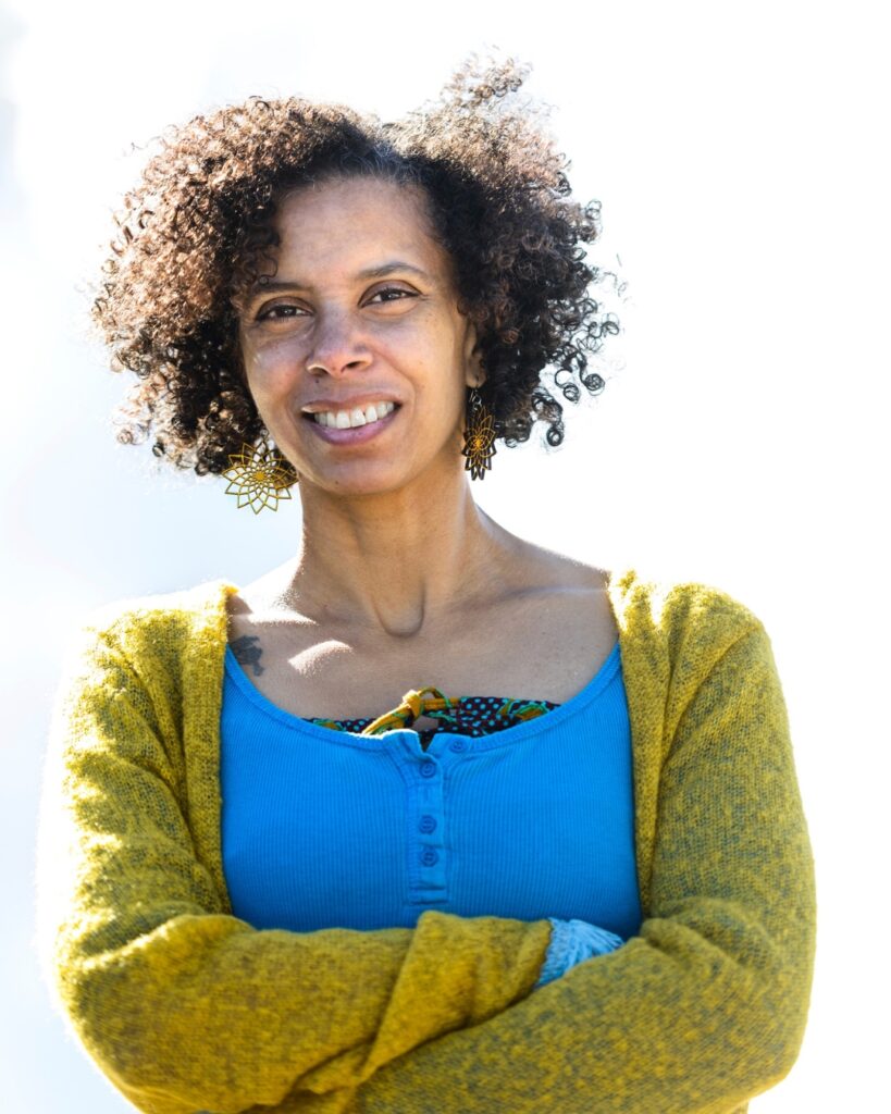 Guest choreographer dr adesola akinleye on reclaiming ballet in her work 'sycorax's tempest' for our centenary insight days Adesola smiles to the camera with her arms crossed. She wears a bright blue top with a yellow-green cardigan.