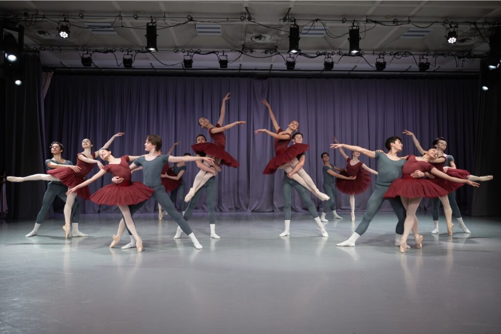 1st year students in red tutus and grey unitards pose in a pas de deux demonstration