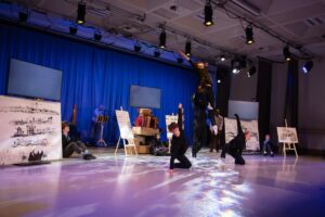 1st year students perform in echo eternal, dressed in all black against a blue backdrop