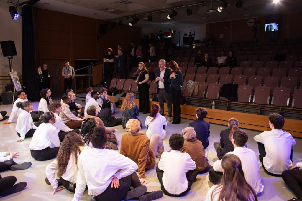 Adrian packer and natasha kaplinsky address the cast of students