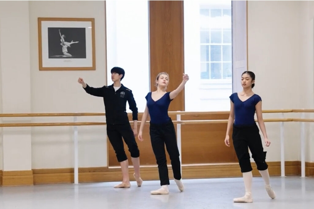 Guest choreographer dr adesola akinleye on reclaiming ballet in her work 'sycorax's tempest' for our centenary insight days Three dancers stand in a diagonal with their eyes closed. A man is in the back, reaching forward mid-step. Two ladies stand next to him, one reaching her left hand to the side and the other facing forward, arms down to her sides. They all are mid-walk with their left legs back.