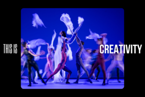 Several dancers on stage in front of a blue background in different colour leotards dancing with pieces of floaty white material.