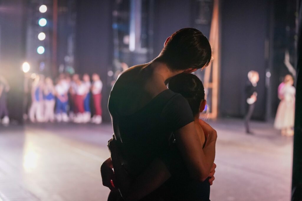 Three longtime supporters of the school share why they choose to leave a lasting legacy for our students Two dancers hug in silhouette backstage with the stage lights in the background. The taller boy leans his head on the shorter girl as they embrace and look at the stage.
