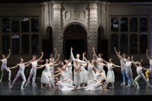 The cast of sweet morning blooms pose in a final group pose at opera holland park. The dancers wear white leotards, tights and long tulle skirts for the ladies. The men have pastel washes of colour on the bottom half of their tights.