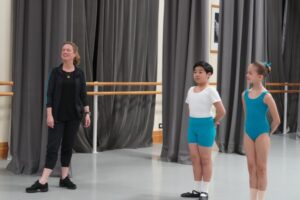 Affiliate artistic manager vanessa donkin vanessa donkin with two young affiliate students. The boy wears a white shirt, teal shorts, white socks and black ballet shoes. The young girl wears a teal leotard, socks that match her skintone and ballet shoes.