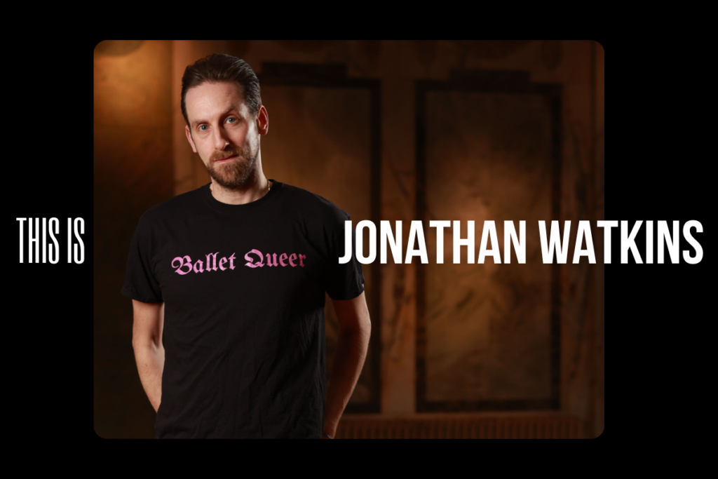 Jonathan standing in a black t-shirt that has his dance company 'ballet queer' written on it in pink.