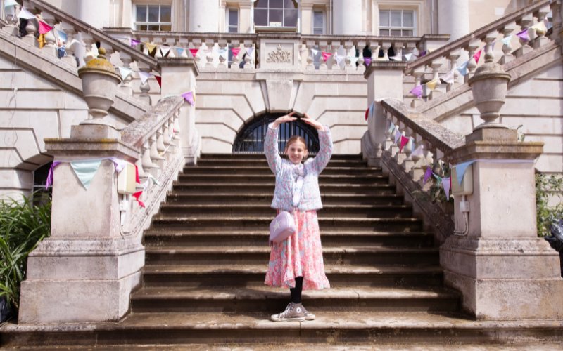 Fair guest posing in a ballet position at the bottom of white lodge steps.