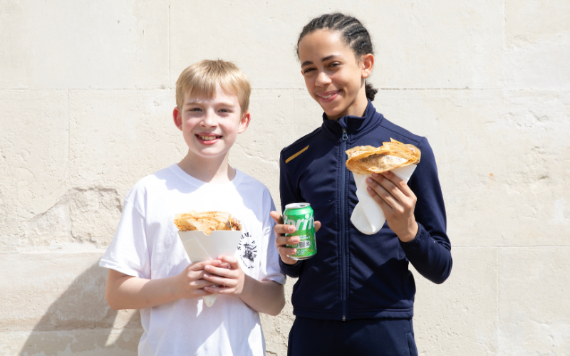 Two students smiling at the fair with crepes in their hands.
