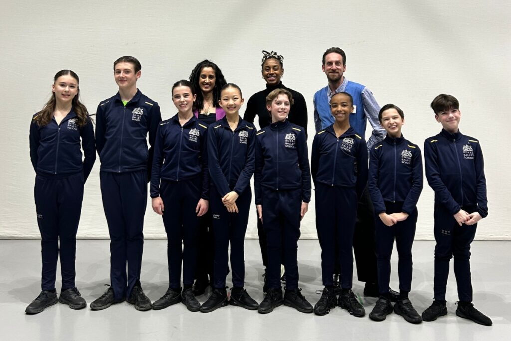 The eight young choreographers stand in matching school tracksuits in front of the three panelists.