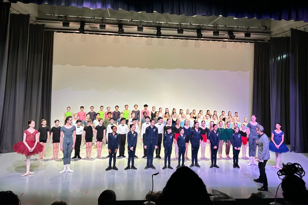 All performers and choreographers stand on the margot fonteyn theatre stage as the audience applauds.