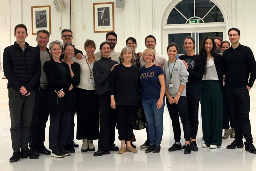 Susan lucas stands front and centre with a group of ballet teachers in the sbs studio at white lodge. They all smile towards the camera.