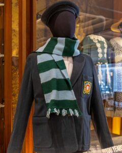 A navy blue blazer with the royal ballet school crest and a scarf wrapped around the neck with light blue and dark green stripes on a black mannequin.